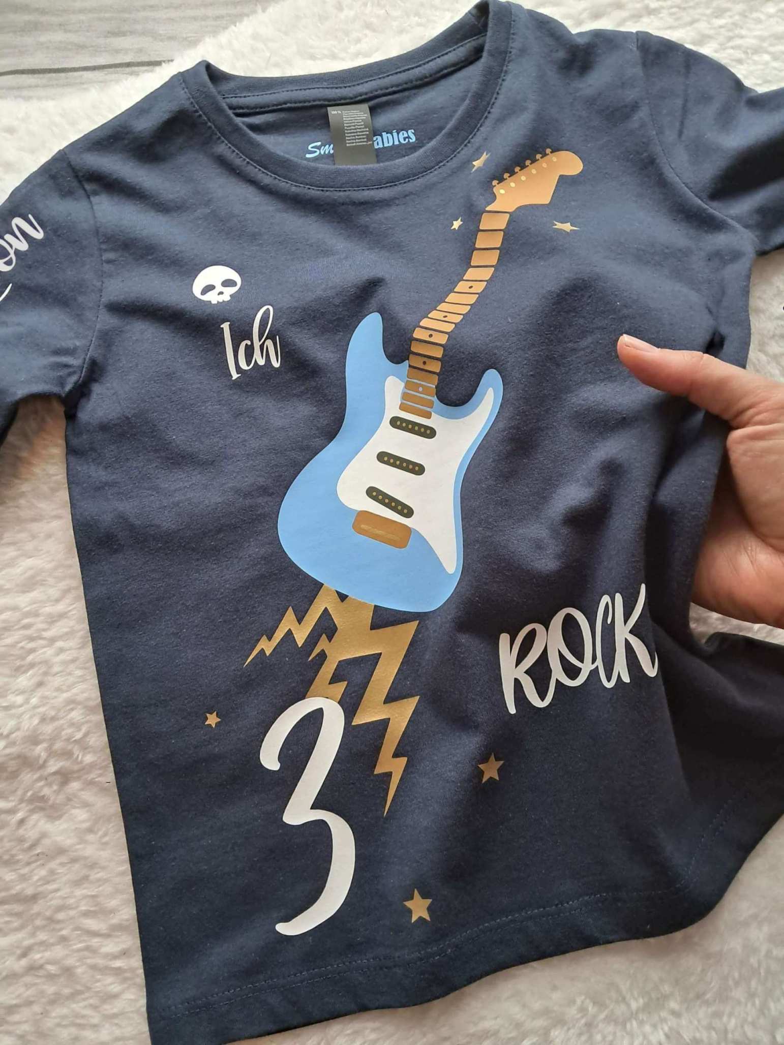 Liegebild von navi Geburtstagsshirt hellblaue E Gitarre für Kinder, mit Zahl und Name, mit gold metallic Effekt