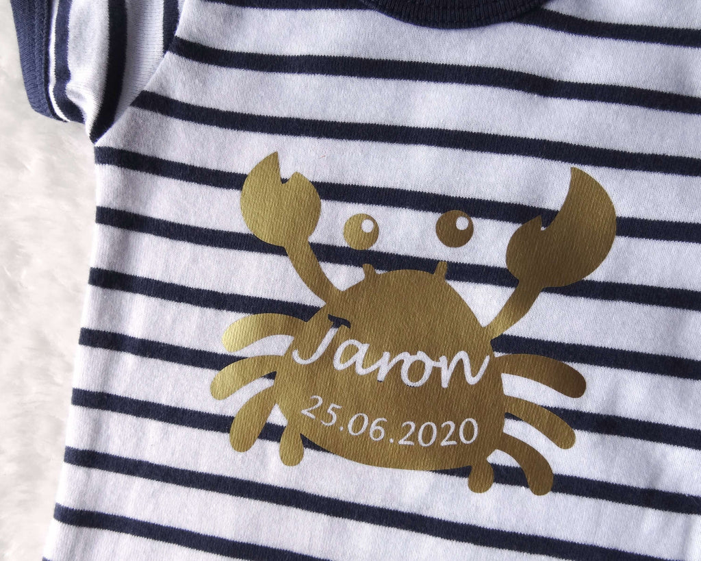 Detailansicht vom goldenen Aufdruck Krabbe mit Geburtsdaten auf gestreiftem Baby-Body