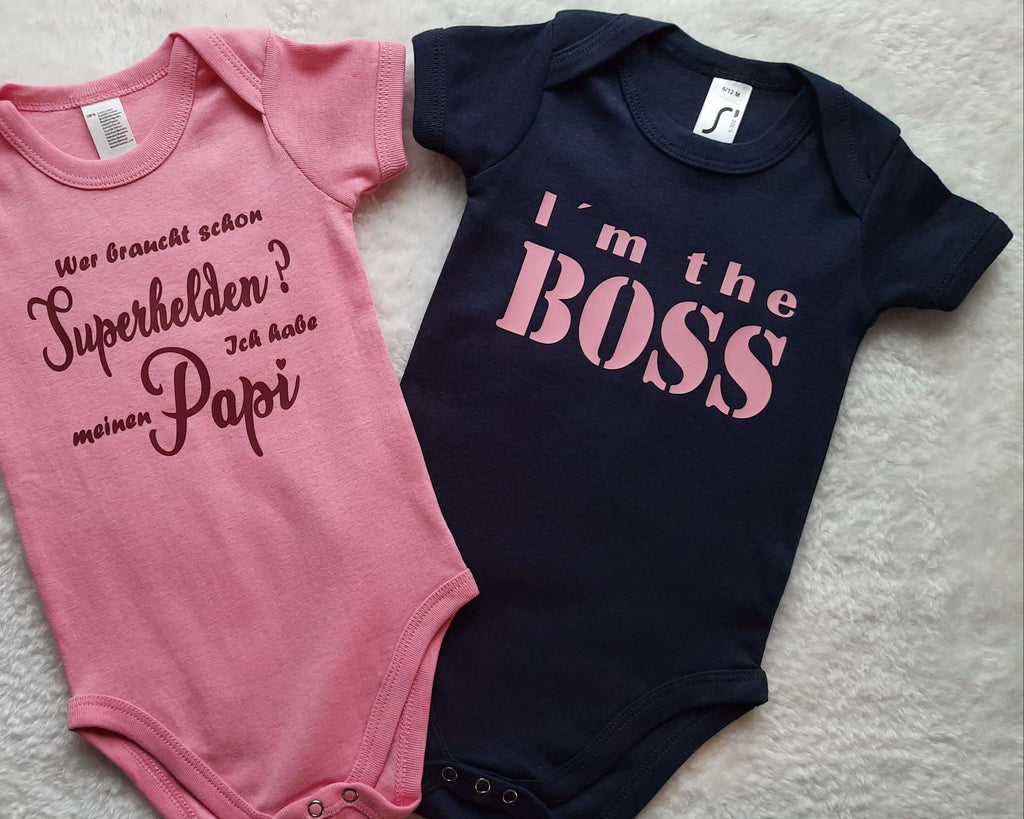 zwei Babybodys von Smartbabies mit I m the Boss in navi und Superheld Papi in rosa