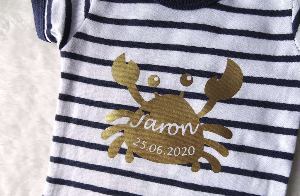 Detailansicht vom goldenen Aufdruck Krabbe mit Geburtsdaten auf gestreiftem Baby-Body
