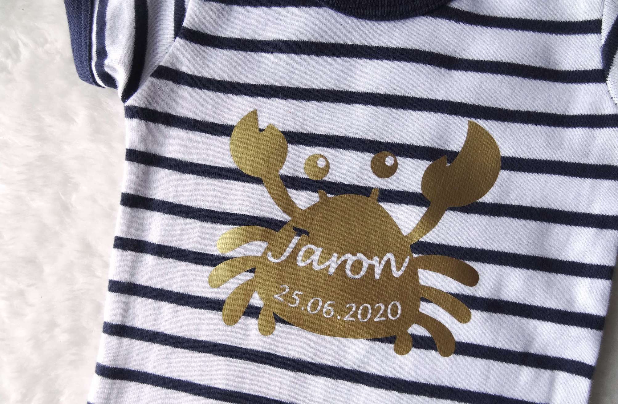 Detailansicht vom goldenen Aufdruck Krabbe mit Geburtsdaten auf gestreiftem Baby-Body