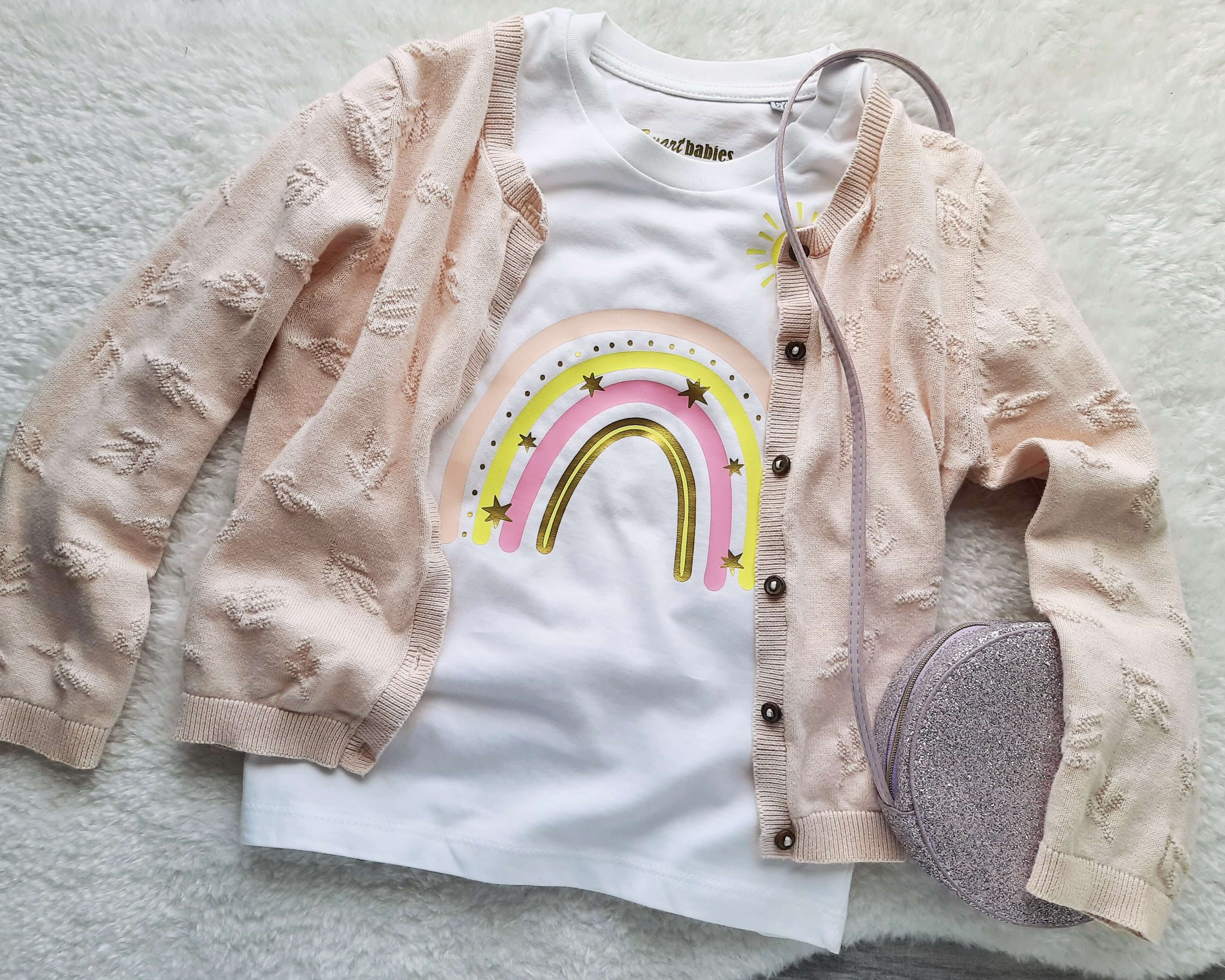 Flatlay Kinder-Langarmshirt in weiß mit Strickjacke, für Geburtstag mit pastell-rosa Regenbogen, Name und Zahl, Sonne und Wolke bedruckt