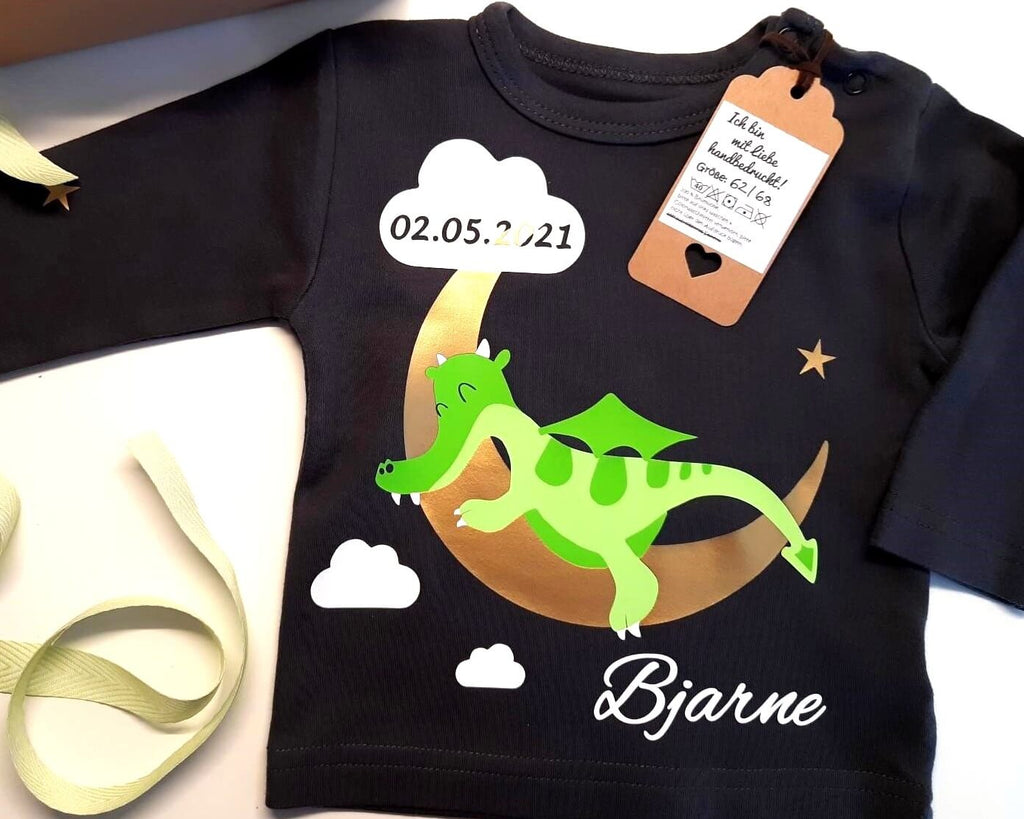 Flatlay dunkelblaues Babyshirt bedruckt mit schlafendem grünem Drache auf goldenem Mond, lange Ärmel und Druckknöpfe