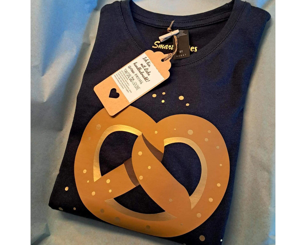 verpacktes navi farbenes Kindershirt, bedruckt mit bayrischer Brezel und gold Tupfen mit Etikett