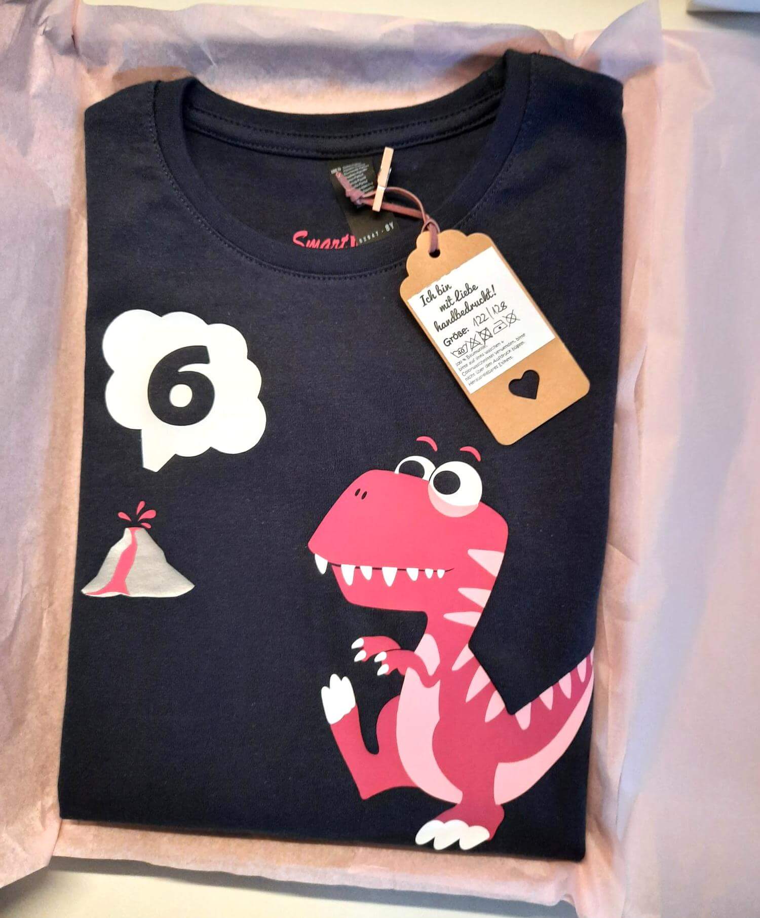 navi farbenes Geburtstagsshirt in Verpackung mit Etikett, bedruckt mit T Rex in rosa-pink, mit Name und Zahl