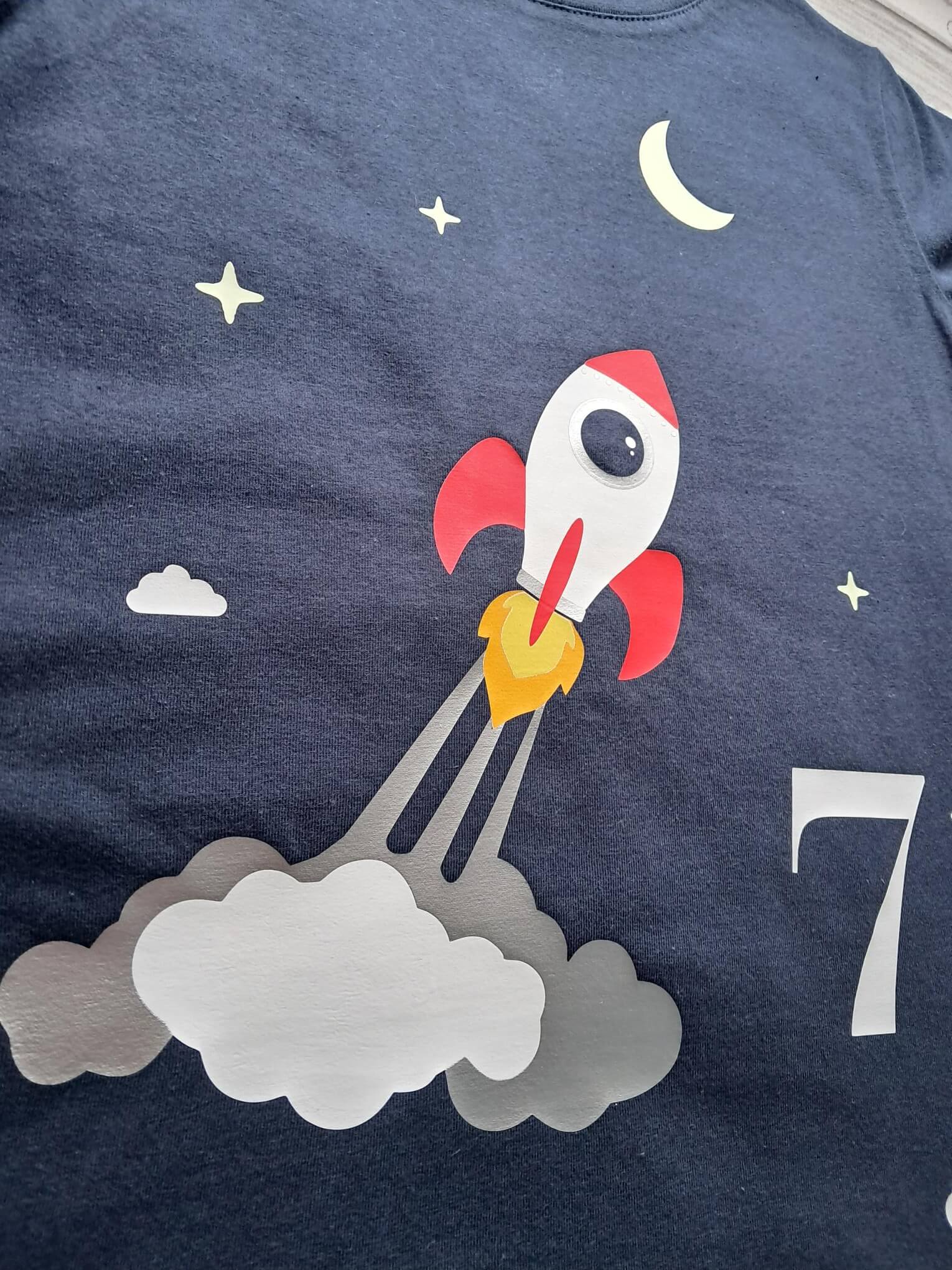 nahe Detailansicht navi Kinder Geburtstagsshirt mit startender Rakete bedruckt, mit Leuchteffekt im Dunkeln, kurze Ärmel