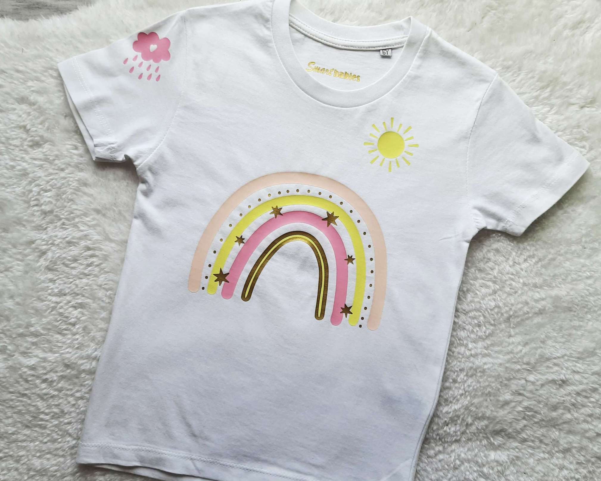Detailansicht Kinder-Kurzarmshirt in weiß für Geburtstag mit pastell-rosaRegenbogen, Name und Zahl, Sonne und Wolke bedruckt