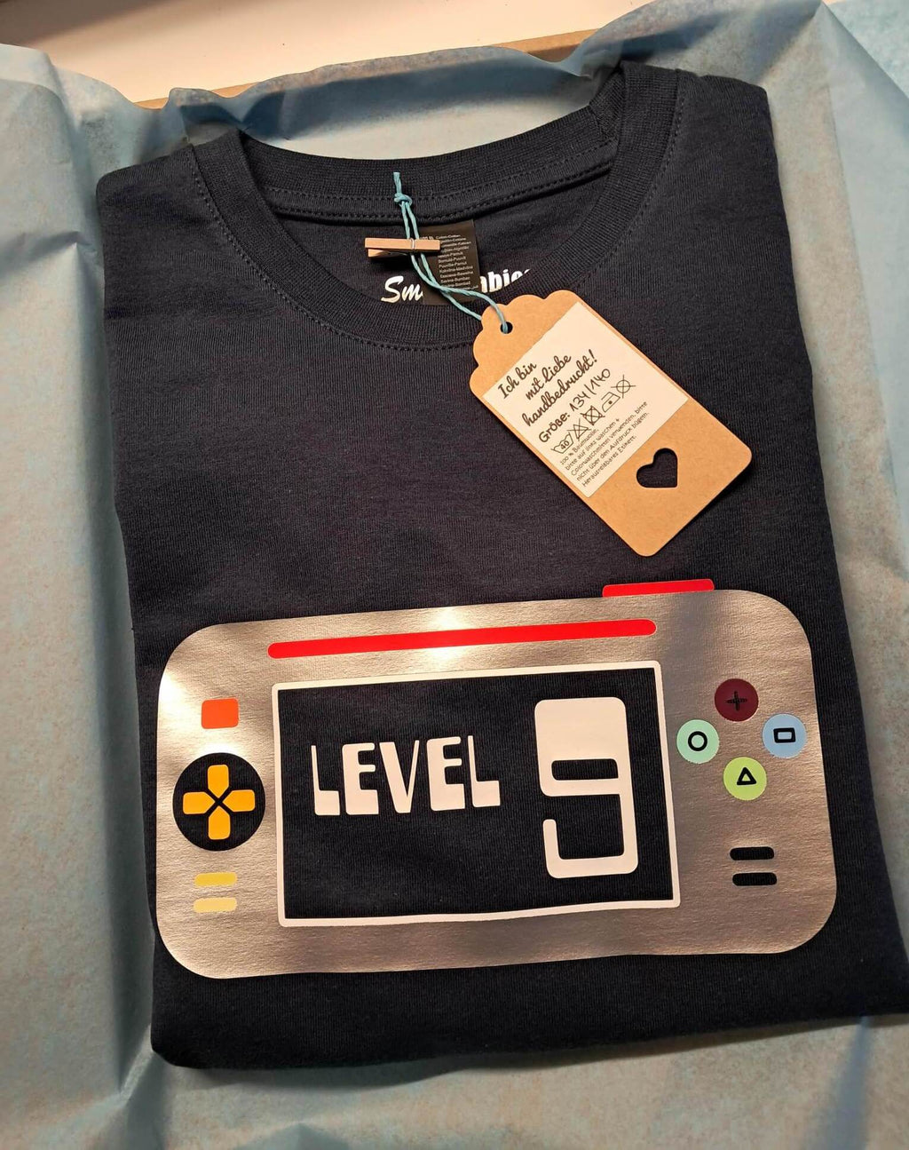 Verpackung von navi Geburtstagsshirt mit Aufdruck Game Konsole, mit Name und Zahl in schimmerndem silber Metallic Effekt