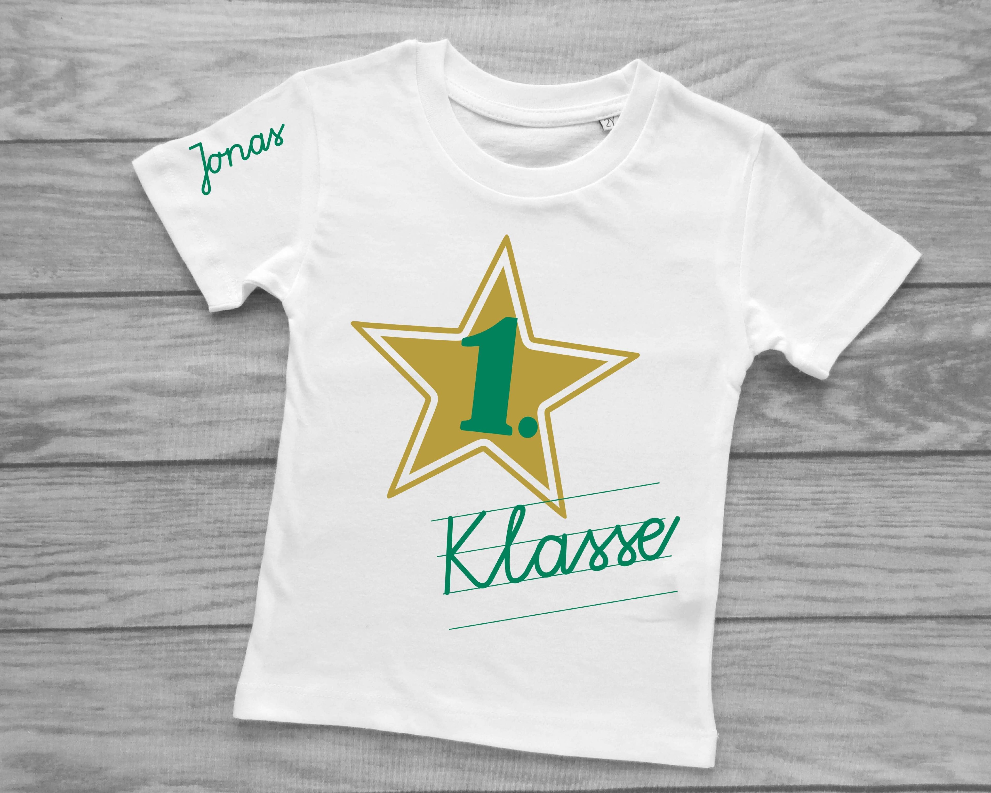 weißes T-Shirt für Einschulung, bedruckt mit Schreibschrift 1. Klasse und Name in petrol und goldenem Stern