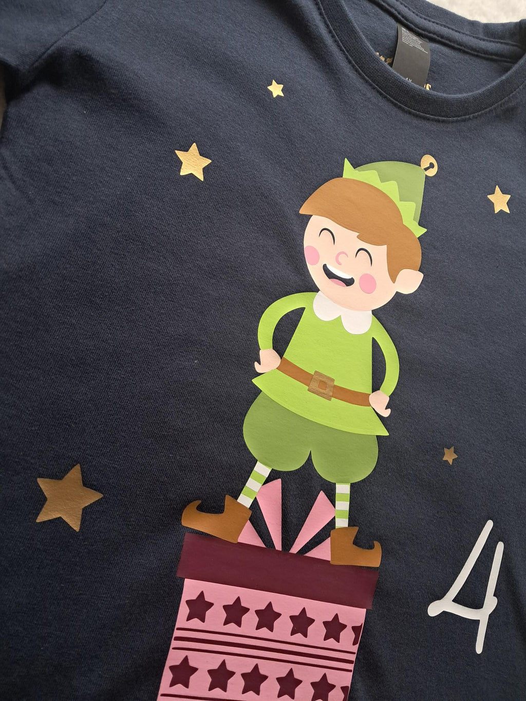 Detail Aufdruck von navi Langarmshirt für Kinder mit Name und Zahl und großem Weihnachtswichtel auf Geschenk stehend